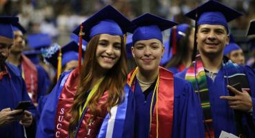 Three TMCC graduates donning blue caps and gowns with colorful sashes and cords gather excitedly for a picture in the Lawlor Events Center arena.