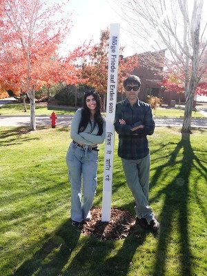 Two international students pose next to the Peace Pole.