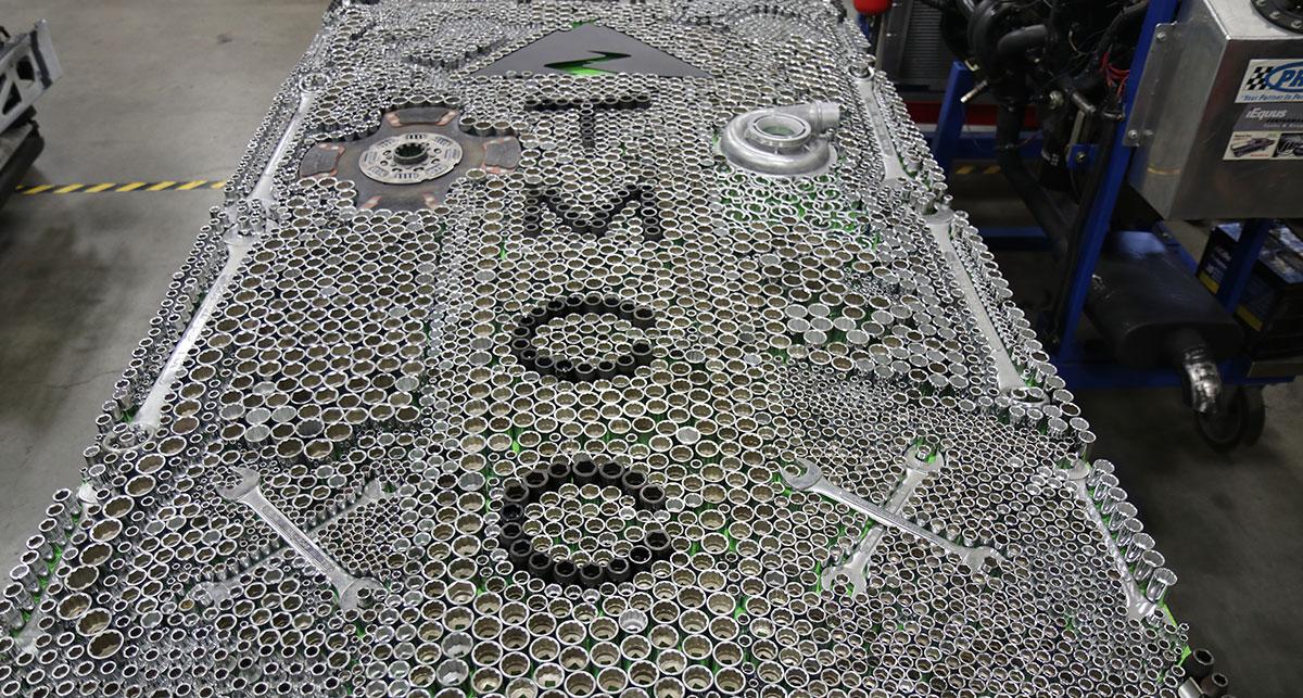 Tools, sprockets, and metal fused into a collage depicting the TMCC logo.