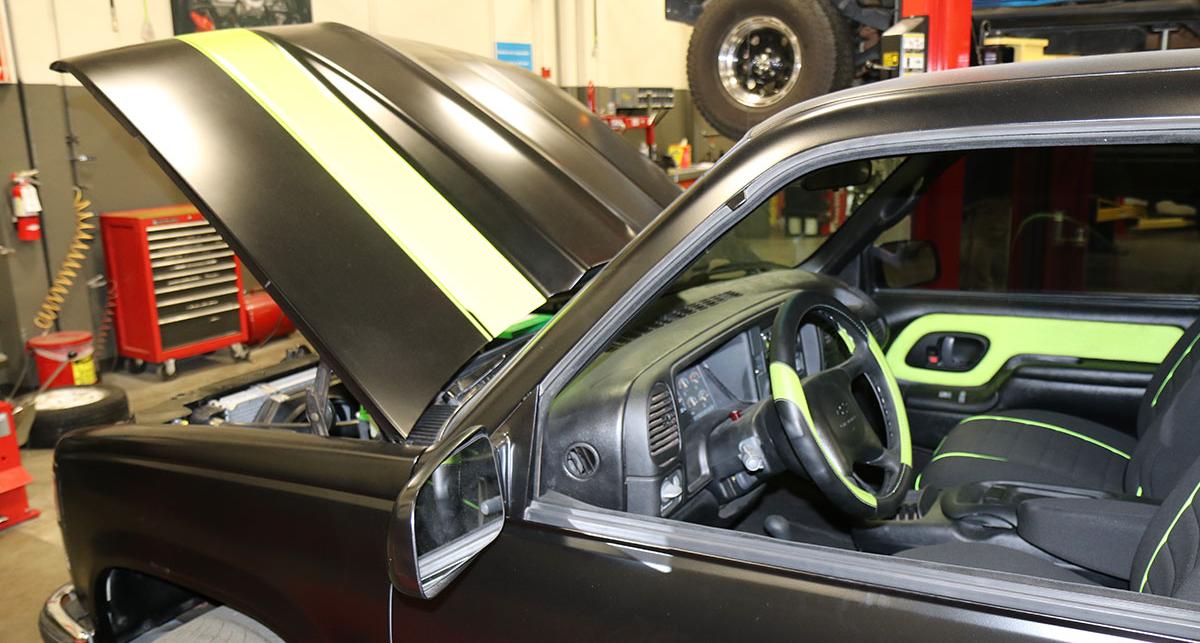 Side view of the black and green truck refurbished by automotive students, with the hood up.