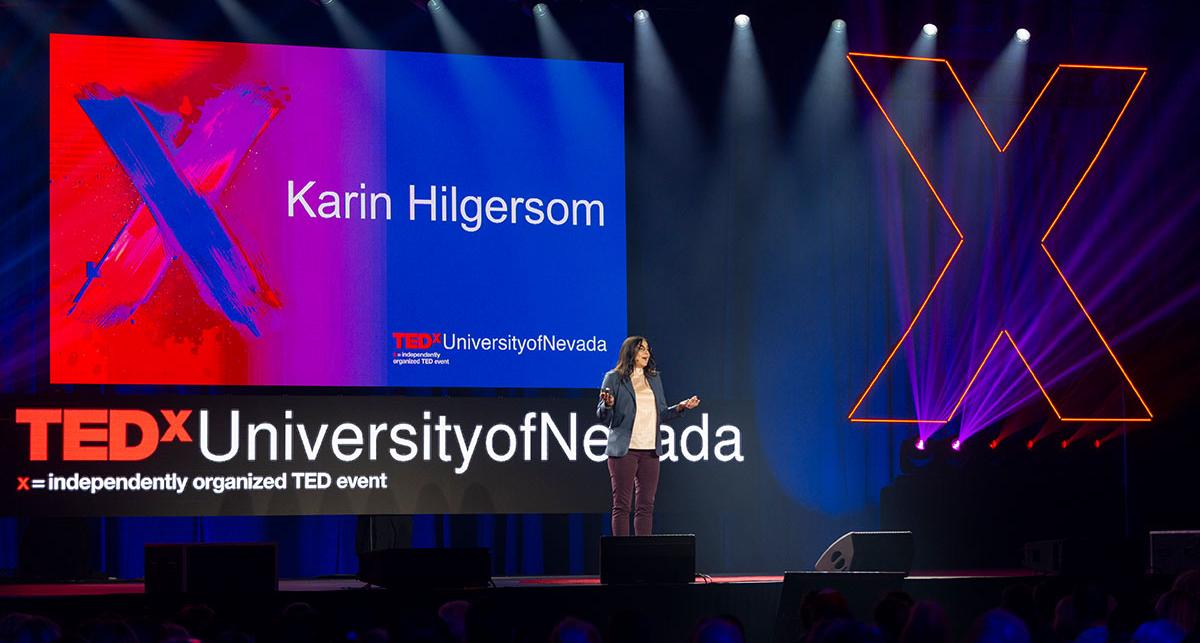 Dr. Karin Hilgersom speaking on stage in front of the TedX screen.