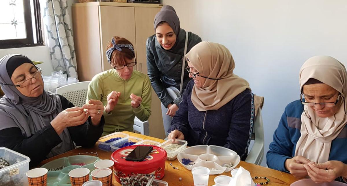 Women sitting around a table, making beaded jewelry.