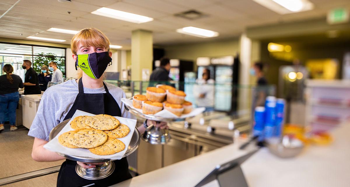 Cafe worker holds trays of baked good.