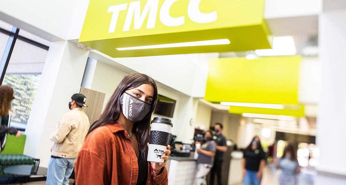 Student with a cup stands in the lobby of the Sierra building.