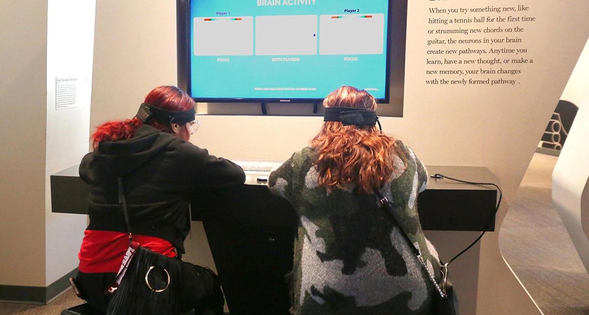 Two students wearing headbands are sat at a desk with a screen in front of them. 