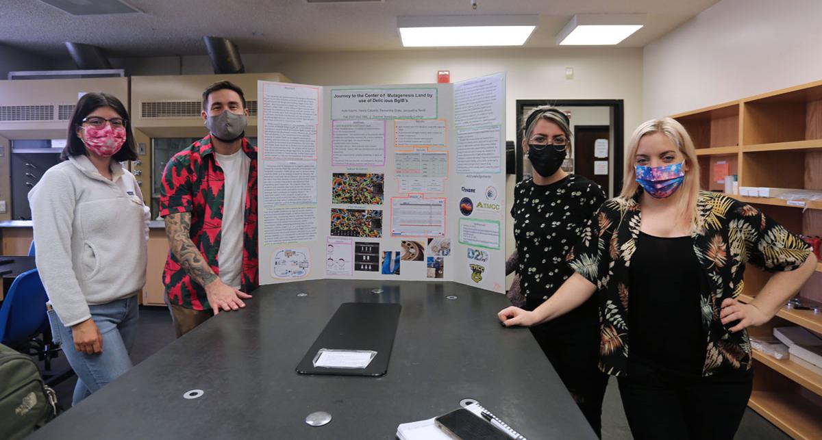 Students pose by research posterboard.