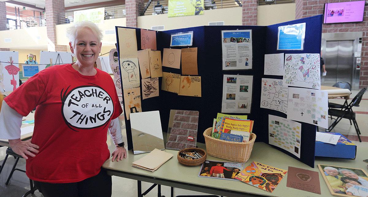 A teacher from the E.L. Cord Child Care Center stands by an art exhibit created by the young children expressing their ideas of identity.