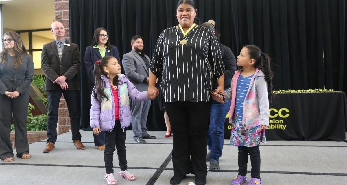 Graduate mother stands proud with her two daughters on the stage.