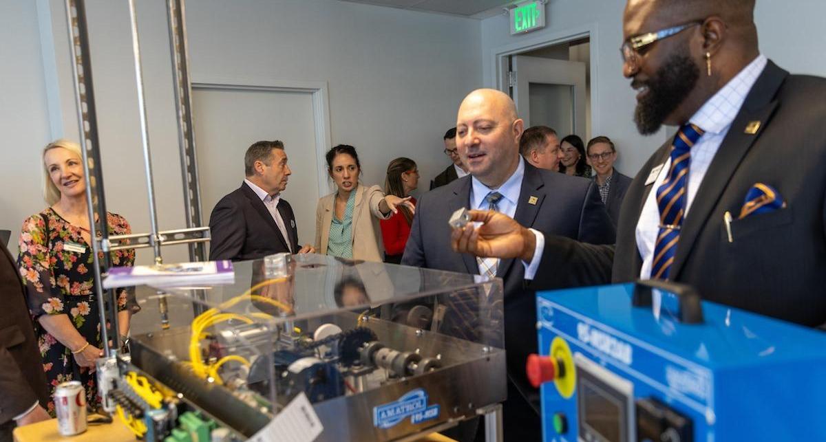 TMCC's Mike Peyerl and Dr. Ayodele Akinola inspect parts of a cutting-edge machine among colleagues.