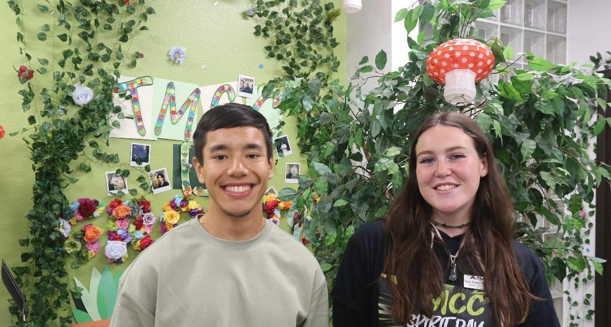 Ayden Rodriguez and Taylor Easley smile for a photo within their gorgeous, mystical forest-themed decorated office.