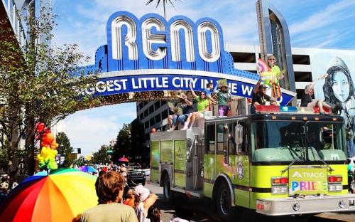 While onlookers cheer, the TMCC green firetruck, with PRIDE written in bold, rainbow letters upfront, moves under the downtown Reno archway with leadership, faculty, and students waving during the parade.