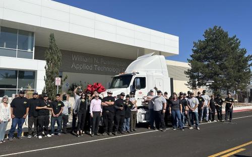 Students, faculty, staff, and partners smile for a group photo beside a milky driver's truck cabin adorning the TMCC logo on the street outside the William N. Pennington Technology Center.