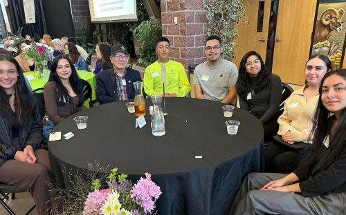 A diverse group of students sits smiling beside their donors at a table inside the Student Center, awaiting the Legacy Scholarship Reception to begin.