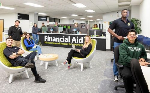 Students in the Financial Aid, Scholarships, and Student Employment Office smile for a photograph while organizing necessary documents for enrollment.