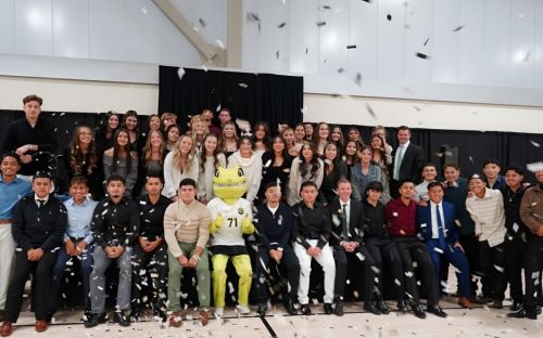 Student-athletes from the Men's and Women's Soccer teams pose for a photo with their coaches and Mighty the Lizard while confetti falls.