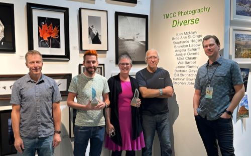 Candace Garlock stands beside colleagues in the Visual and Performing Arts Program, holding her award. Mesmerizing imagery is behind her on the wall.