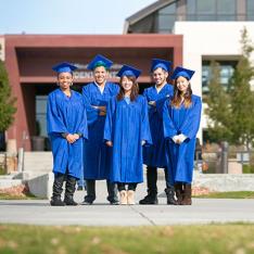 Students in cap and gown standing in front of building