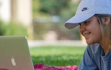 Student looks at her laptop computer outdoors.