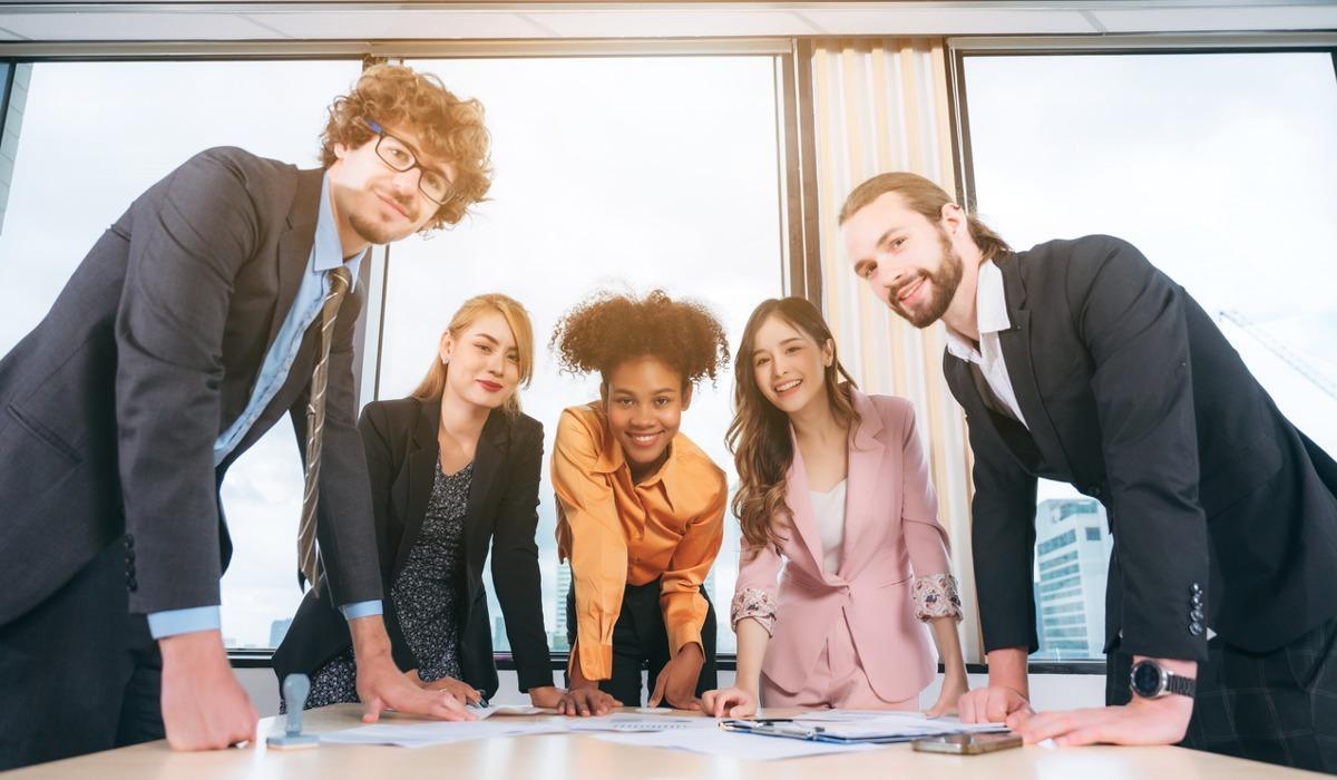 Five multicultural business students gather around a table in a high-rise building while sharing research.