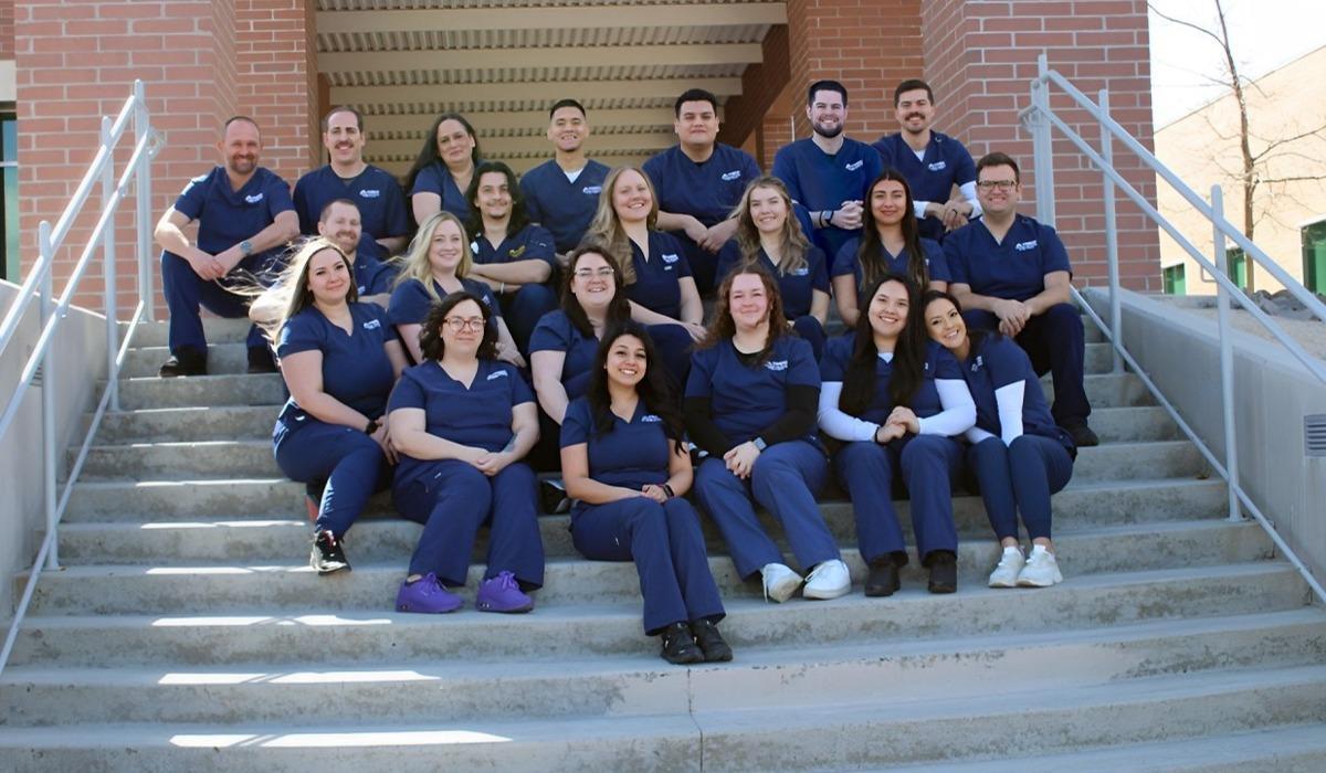 The 2024 Radiologic Technology class smiles while seated, wearing navy blue scrubs, posing for a photograph on the steps of the William N. Pennington Health Science Center.