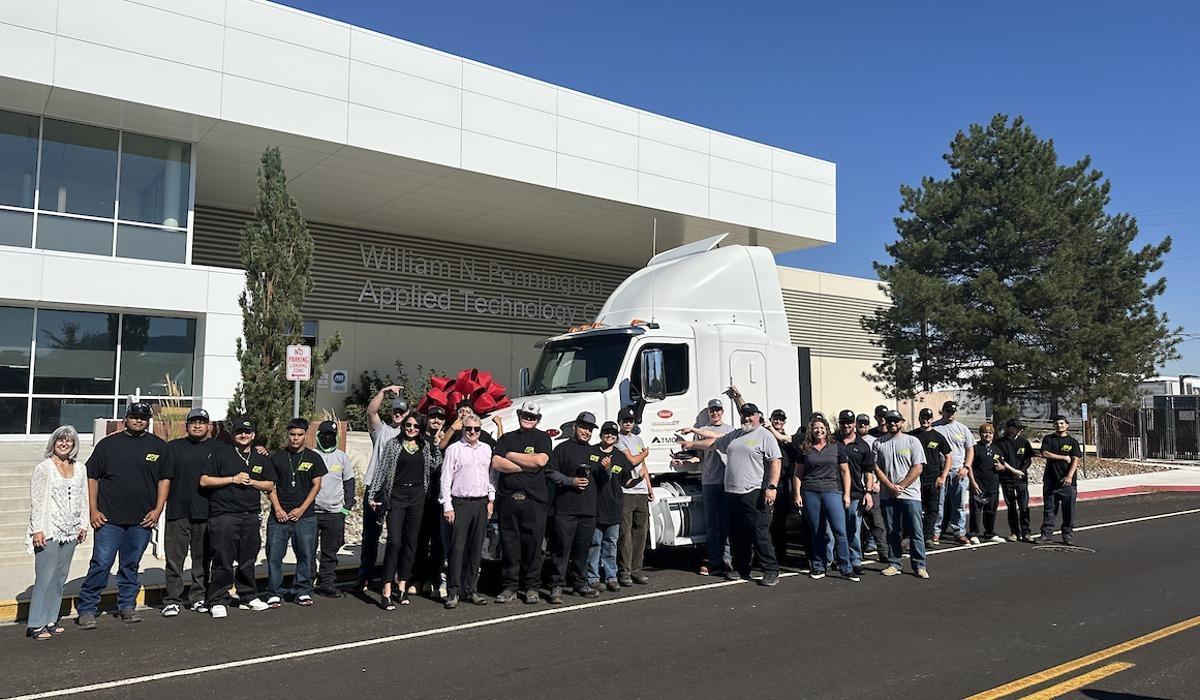 Students, faculty, staff, and partners smile for a group photo beside a milky driver's truck cabin adorning the TMCC logo on the street outside the William N. Pennington Technology Center.