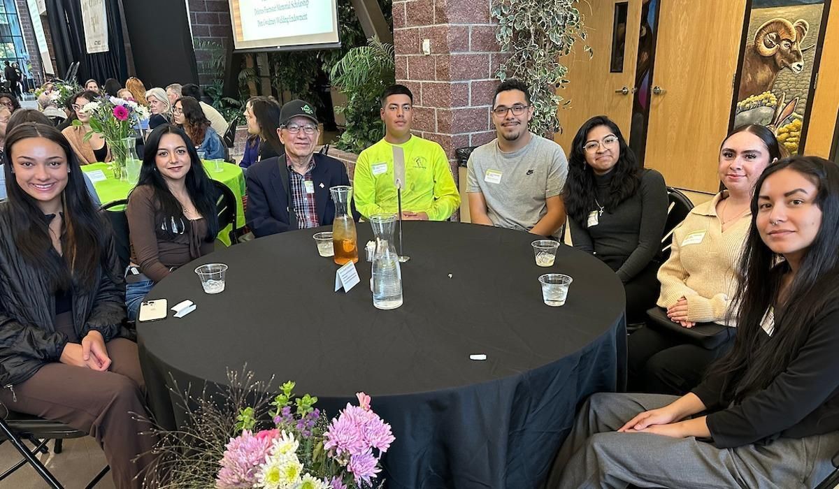 A diverse group of students sits smiling beside their donors at a table inside the Student Center, awaiting the Legacy Scholarship Reception to begin.