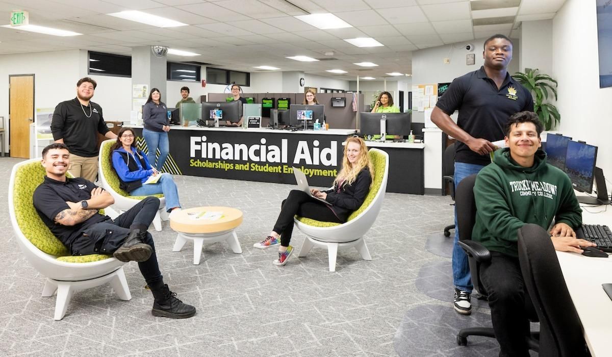 Students in the Financial Aid, Scholarships, and Student Employment Office smile for a photograph while organizing necessary documents for enrollment.