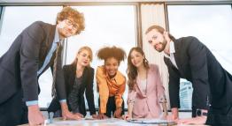 Five multicultural business students gather around a table in a high-rise building while sharing research.