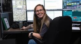 An emergency dispatch responder smiles while sitting behind her six computer screens, monitoring incoming or outgoing calls.