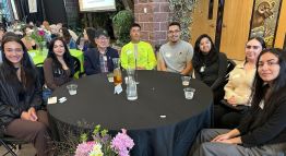 A diverse group of students sits smiling beside their donors at a table inside the Student Center, awaiting the Legacy Scholarship Reception to begin.