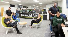 Students in the Financial Aid, Scholarships, and Student Employment Office smile for a photograph while organizing necessary documents for enrollment.